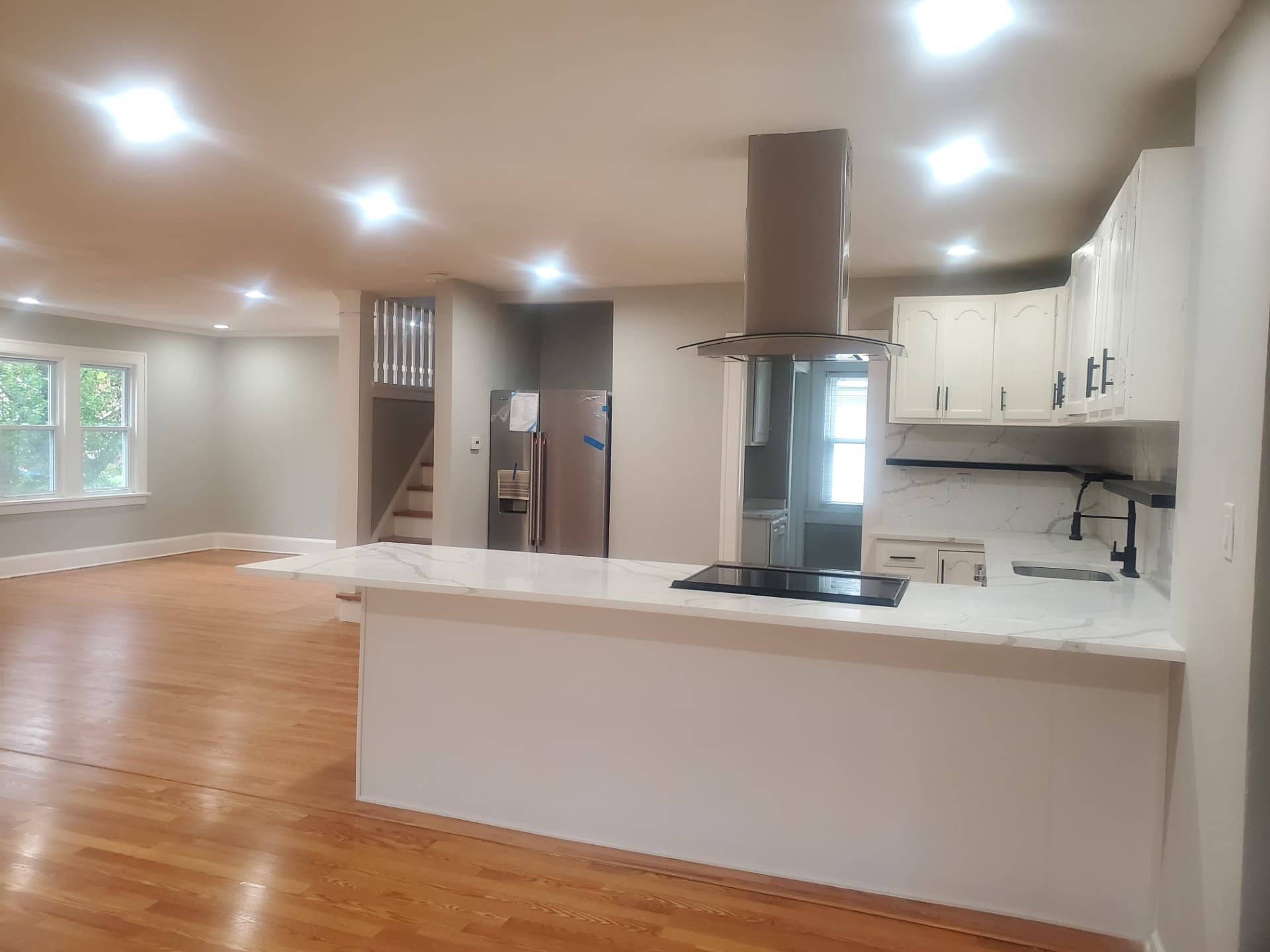 Finished kitchen with white cabinetry, quartz waterfall counters, and island hood