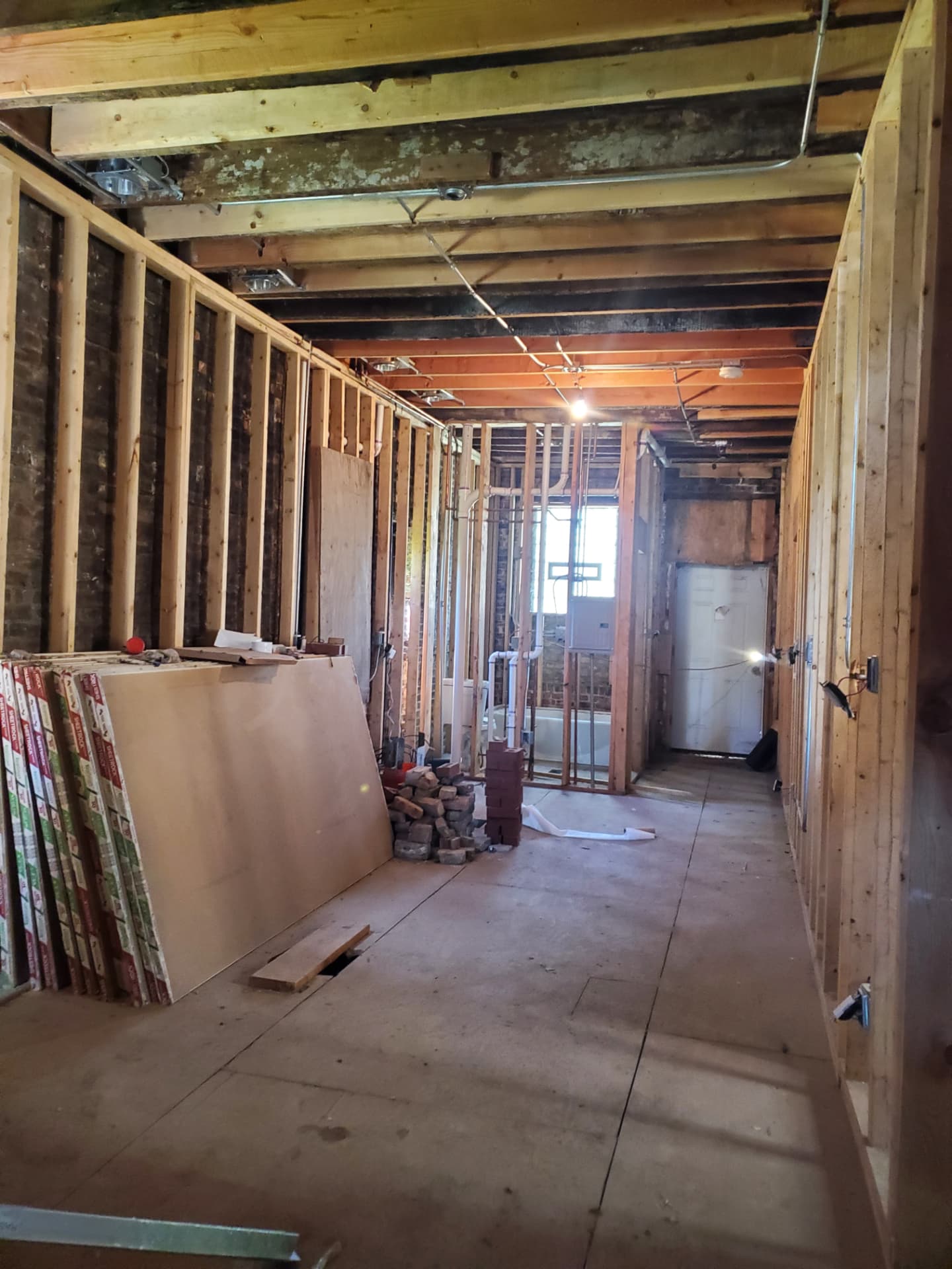 Long open interior with new framing, rough plumbing, and drywall staged for install